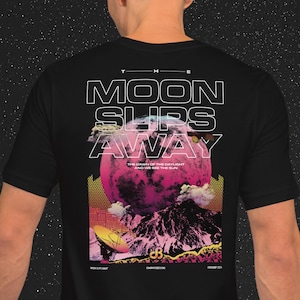 Puede incluir: Camiseta negra con un estampado gráfico de una luna rosa, montañas y una antena parabólica. El texto "THE MOON SLIPS AWAY" está impreso en blanco en la camiseta. El texto "THE DAWN OF THE DAYLIGHT AND WE SEE THE SUN" está impreso en blanco debajo de la luna.