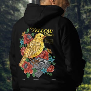 May include: Black hoodie with a yellow bird illustration on the back. The bird is perched on a music mixer with flowers and leaves surrounding it. The text "YELLOW BIRD" is above the bird and the text "Pretty Lights" is on the mixer.
