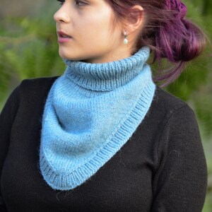 May include: A light blue knitted cowl neck scarf with a folded edge. The scarf is worn by a person with purple hair.