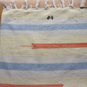 May include: A woven rug with a striped pattern in shades of yellow, blue, and orange. The rug has a fringe border and the number "#4" is written in the center.