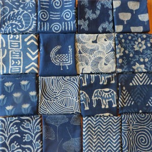 May include: An assortment of indigo blue fabric squares with white patterns. The designs include floral, geometric, and animal motifs. The squares are arranged in a grid, showcasing the variety of patterns.