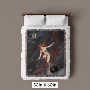 May include: A woven tapestry throw blanket featuring a vintage illustration of a woman flying on a broomstick with a black cat. The woman is wearing a red robe and has long red hair. The background is a dark blue night sky with stars and a crescent moon.