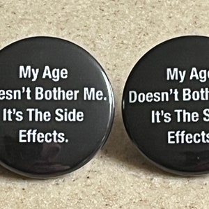 May include: Two black round buttons with white text that reads "My Age Doesn't Bother Me. It's The Side Effects."