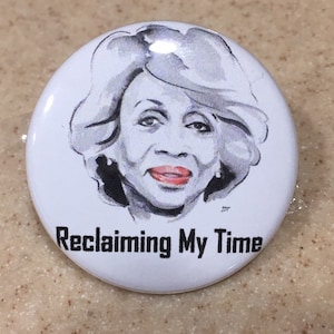 Op de afbeelding: Een witte knop met een zwart-witte illustratie van een vrouw met grijs haar. De tekst "Reclaiming My Time" is in zwart onder de illustratie gedrukt.