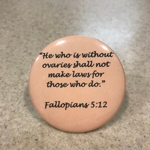 May include: A round, peach-colored button with a black quote that reads "He who is without ovaries shall not make laws for those who do." The quote is attributed to "Fallopians 5:12".