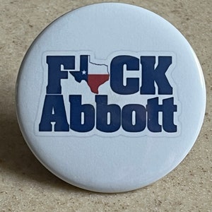 Puede incluir: Un botón blanco con una pegatina azul y roja que dice "F*CK Abbott" con un contorno de la bandera de Texas.