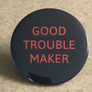 以下が含まれることがあります： 赤い文字で「GOOD TROUBLE MAKER」と書かれた黒いボタン