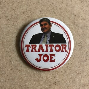 May include: A white button with a red border and a picture of a man in a suit. The text "TRAITOR JOE" is written in red letters.