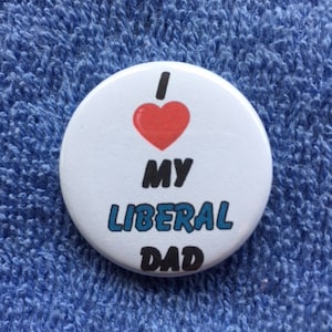 Puede incluir: Botón blanco con un corazón rojo y el texto "Amo a mi padre liberal" en letras negras y azules.