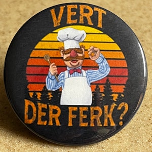 Op de afbeelding: Een zwarte en oranje knop met een retro zonsondergang achtergrond. Een cartoonkok met een witte koksmuts, rode neus en een snor houdt een houten lepel en een klein oranje voorwerp vast. De tekst "VERT DER FERK?" is op de knop gedrukt.