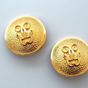 Könnte beinhalten: Ein Paar goldfarbene Ohrringe mit einer strukturierten Oberfläche und einem erhabenen, stilisierten 'L'-Design.