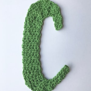 May include: A green crocheted letter C. The letter is made with a single crochet stitch and is a light green color.