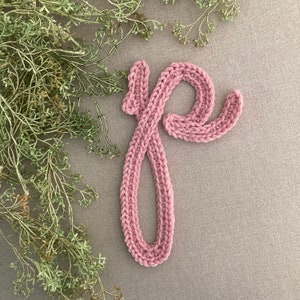 May include: A pink knitted letter "p" on a gray background.