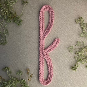 May include: A pink knitted headband with a unique design resembling antlers. The headband is made of soft yarn and has a delicate, feminine look.