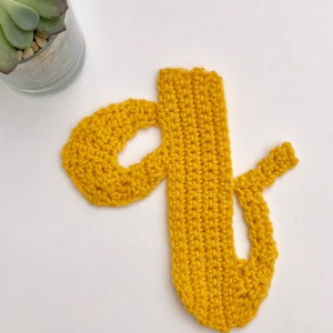 May include: A crocheted letter "d" in a bright yellow color. The letter is made with a single crochet stitch and has a slightly textured surface.