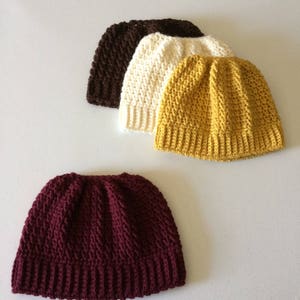 May include: Four crocheted hats in different colors: brown, white, yellow, and burgundy. The hats are all the same style, with a simple, ribbed design.
