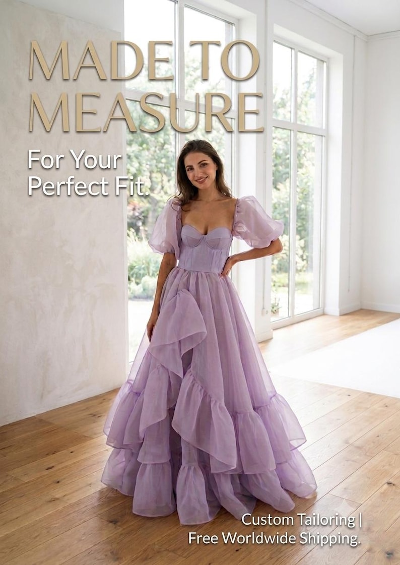 May include: A floor-length lavender gown featuring a structured corset-style bodice, sheer puff sleeves, and a voluminous skirt with layered ruffles. The text "MADE TO MEASURE For Your Perfect Fit" is visible at the top of the image.