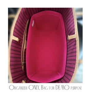 Pu&ograve; includere: Un organizer per borsa in feltro rosa acceso posizionato all'interno di una borsa tote con fodera a righe rosa scuro e nere. L'organizer presenta una forma rettangolare con angoli arrotondati e una piccola etichetta bianca sul lato.