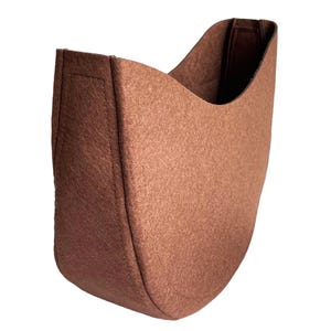 May include: A brown felt fabric planter with a curved shape. The planter is designed to be hung on a wall.