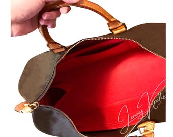 May include: Open view of a brown duffel bag with a red interior. The bag has a zipper closure and tan leather handles and trim. The bag is held open by a hand.
