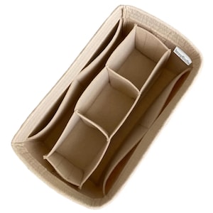 May include: Beige felt handbag organiser with multiple compartments. The organiser has a rectangular shape with several interior pockets and dividers to keep items organised. The product is designed to fit inside a handbag and has a label that reads "JennyKraftz".