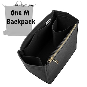 Peut inclure: Un organisateur de sac à dos en feutre gris foncé avec plusieurs compartiments intérieurs et une fermeture éclair en métal doré. Le graphique en arrière-plan affiche le texte 'DESIGNED FOR One M Backpack' pour indiquer la compatibilité.