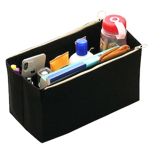 Puede incluir: Organizador de fieltro negro con m&uacute;ltiples compartimentos para un bolso de mano. El organizador est&aacute; lleno de art&iacute;culos como un tel&eacute;fono, loci&oacute;n, bol&iacute;grafos y una botella de agua.
