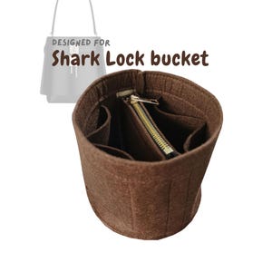 May include: A brown felt bag organizer with multiple compartments and a zippered pocket. The text "DESIGNED FOR Shark Lock bucket" is visible in the image. The organizer is designed to fit inside a Shark Lock bucket bag.