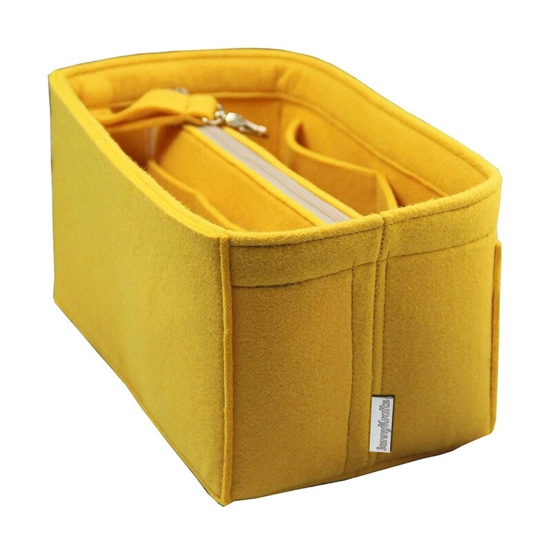 May include: A mustard yellow felt bag organiser with multiple compartments and a zipped pocket. The organiser has a rectangular shape with a structured design and a small label on the side.
