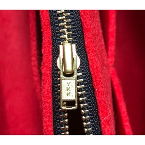Pode incluir: Close-up de um z&iacute;per dourado com dentes pretos e um fundo de tecido vermelho. O puxador do z&iacute;per tem o texto "YKK" gravado.