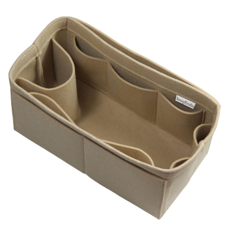 May include: A beige felt handbag organizer insert with a rectangular shape, featuring multiple interior compartments of varying sizes and a cylindrical side pocket. A small white fabric tag with the text "JennyKraft" is attached to the interior.