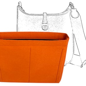 Puede incluir: Un organizador de bolso de mano de fieltro naranja con una cremallera negra, diseñado para encajar dentro de un bolso de hombro. El organizador tiene múltiples compartimentos y se muestra delante de un dibujo lineal de un bolso de hombro.