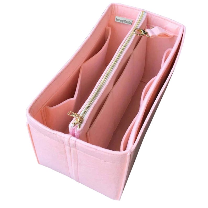 May include: A light pink felt bag organiser with multiple compartments and a zipped central section. The organiser has a gold-coloured zip and hardware. The brand name "LoveyKrafts" is printed on a small white label.