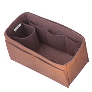 May include: A brown felt handbag organizer insert with a rectangular shape, featuring multiple interior compartments and pockets of varying sizes for storage. A small white fabric tag with the text "JennyKraft" is attached to the inner side.