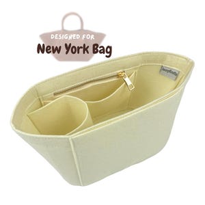 Puede incluir: Un organizador de bolso de fieltro color crema con varios bolsillos y un compartimento con cremallera. El organizador está diseñado para el bolso New York y tiene una pequeña etiqueta que dice "Jenny&Kaitlin".