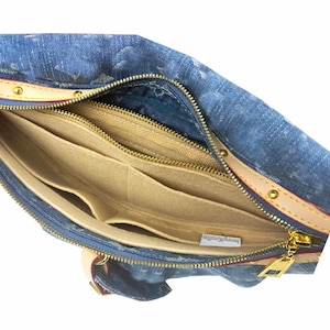 Könnte beinhalten: Blaue Jeans-Handtasche mit goldenem Reißverschluss und beigefarbenen Lederriemen. Der Innenraum verfügt über mehrere beige Filzfächer. Die Tasche ist offen und zeigt das Innendesign und die Konstruktion.