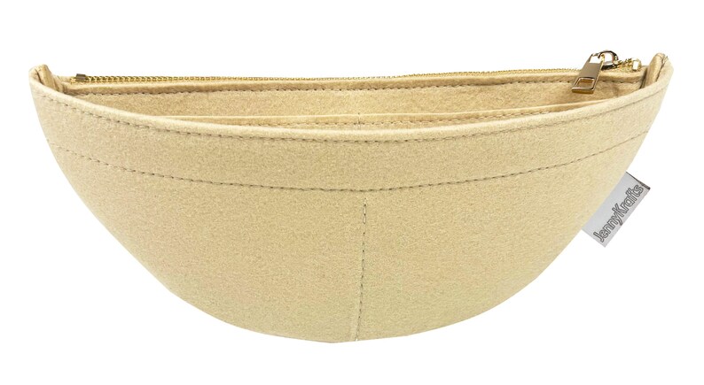 May include: A beige felt handbag organizer with a curved shape and a gold zipper closure. The organizer has multiple compartments and a small tag that reads "jennyKrafts".