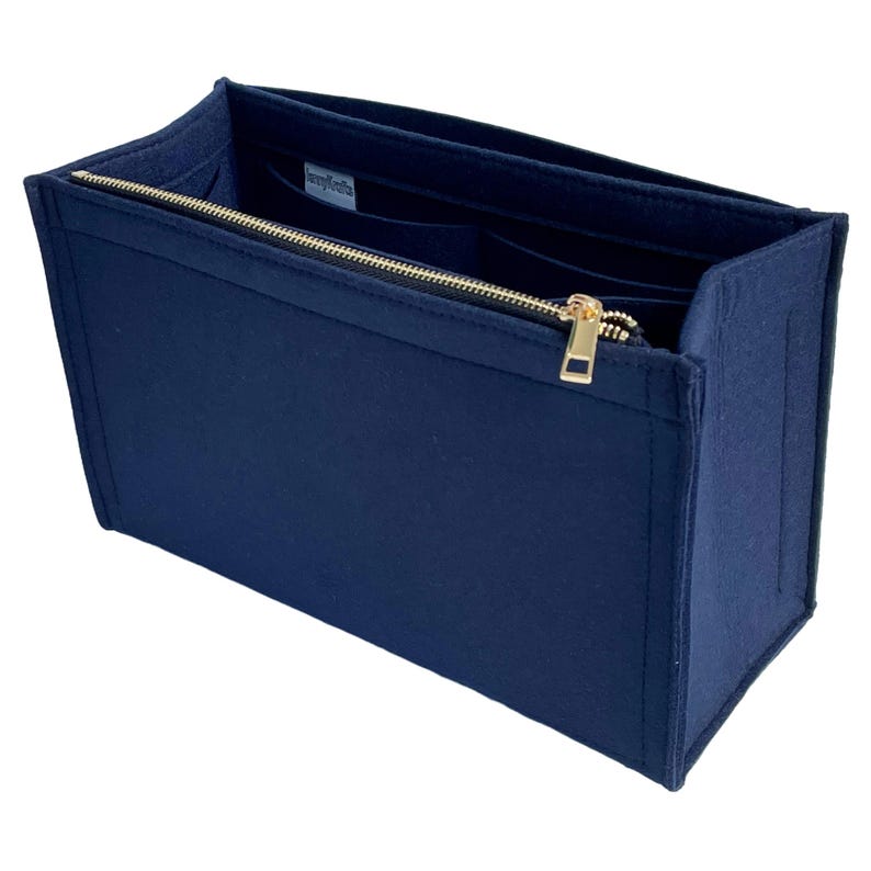 Op de afbeelding: Een marineblauwe vilten handtassenorganizer met een goudkleurige ritssluiting. De organizer heeft meerdere compartimenten en is ontworpen om in een grotere tas te passen. De ritssluiting loopt over de bovenkant.