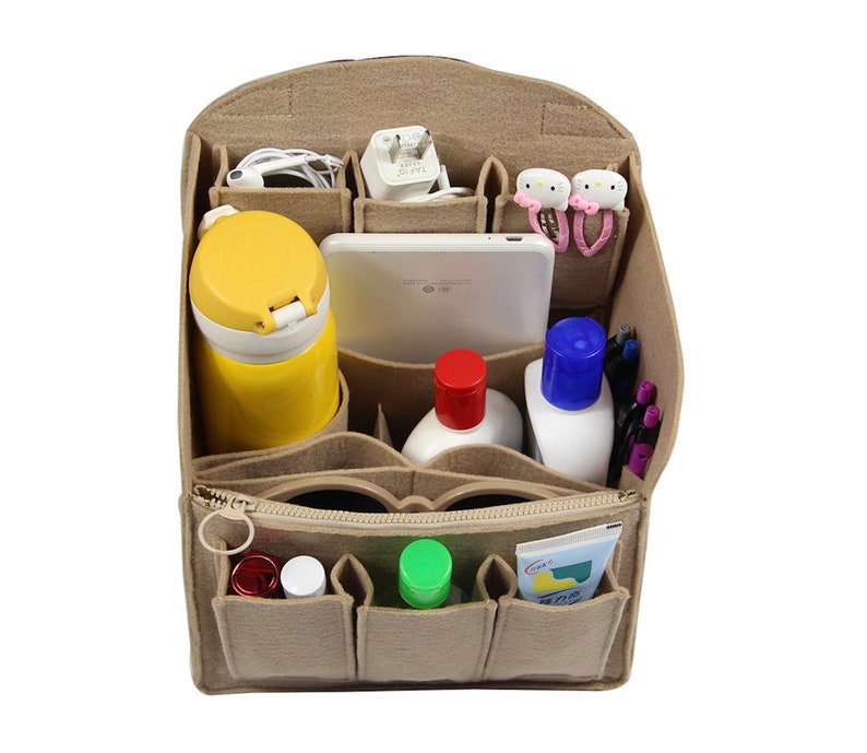 Op de afbeelding: Beige felt organizer met meerdere vakken voor een handtas of schoudertas. De organizer is gevuld met verschillende items, waaronder een waterfles, een tablet, een telefoonlader, handdesinfectie, lotion, pennen en elastiekjes voor haar.