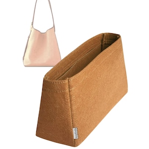 May include: A tan felt handbag organizer with a rectangular shape and angled sides. The organizer has a small label on the side and is designed to fit inside a handbag. A light pink handbag is visible in the background.