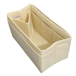 May include: A cream-colored rectangular felt bag organizer insert featuring multiple interior and exterior pockets for storage. The interior includes a central divider and a small white fabric tag with the text SavvyCrafts printed in black.