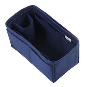 May include: A rectangular navy blue felt bag organizer insert featuring multiple interior compartments and dividers. The structure is open-topped with a small white fabric tag on the inner side wall that displays the text SavvyKraft.