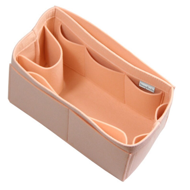 May include: A peach-colored felt handbag organizer insert featuring multiple interior compartments and pockets of varying sizes. The rectangular structure includes a small white fabric tag with the text "JennyKrafts" sewn onto the inner side wall.