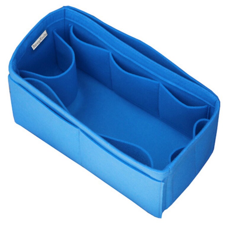 May include: A bright blue felt handbag organizer insert with a rectangular shape, featuring multiple interior compartments and pockets of varying sizes for storage. A small white fabric tag with black text is attached to the inner top edge.