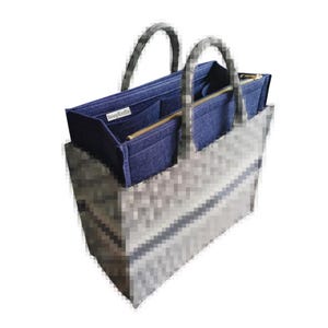 Op de afbeelding: Een grijze draagtas met een blauwe interieur organizer. De tas heeft twee grijze handvatten en een patroon aan de buitenkant. De blauwe organizer heeft meerdere compartimenten en een gouden rits. De organizer heeft een klein wit label.