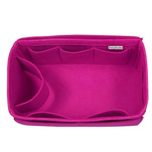May include: A bright fuchsia felt handbag organizer insert featuring a rectangular shape with multiple interior pockets of varying sizes along the sides. A small white rectangular fabric label with the text "JennyKraft" is sewn onto the inner rim.