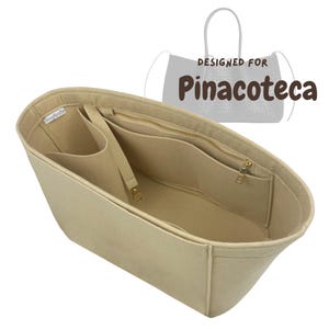 Pode incluir: Um organizador de bolsa em feltro bege com múltiplos compartimentos internos, um bolso com zíper e uma pequena etiqueta de tecido. O gráfico exibe um desenho linear de uma bolsa tote com o texto DESIGNED FOR Pinacoteca acima.