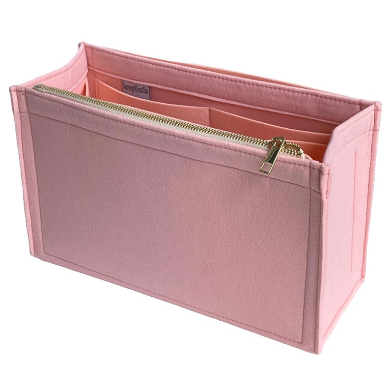 Op de afbeelding: Een lichtroze vilten handtassenorganizer met een gouden rits. De organizer heeft meerdere compartimenten en vakken voor het opbergen van spullen. De binnenkant is een lichtere tint roze. Ontworpen om in een grotere handtas te passen.