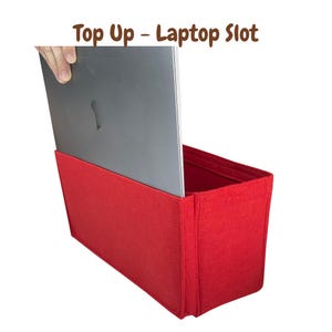 Puede incluir: Organizador de fieltro rojo con una ranura para portátil. El portátil se está insertando en la ranura. El texto "Top Up - Laptop Slot" es visible en la parte superior de la imagen.