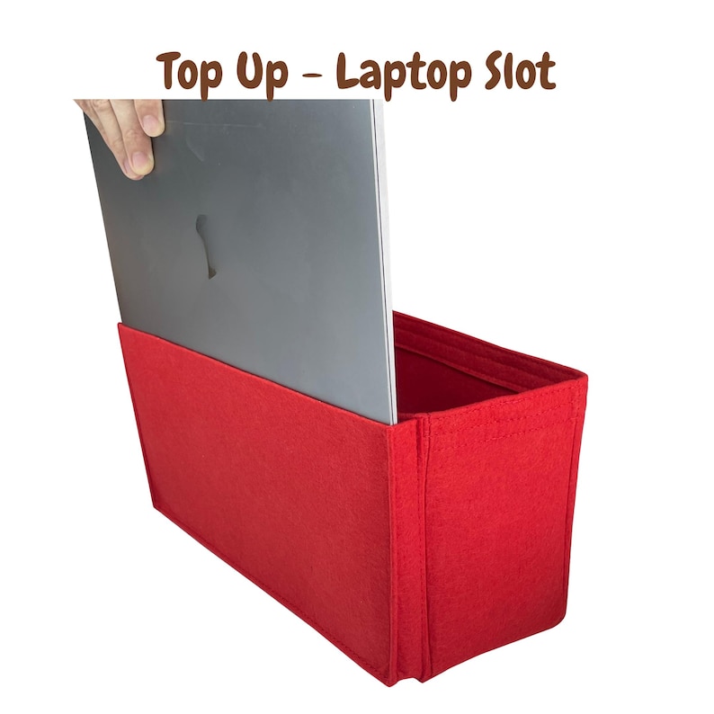 May include: A bright red felt laptop organizer with the text "Top Up - Laptop Slot" in brown. A silver laptop is being inserted into the open top of the organizer. The organizer is rectangular and designed to hold a laptop.